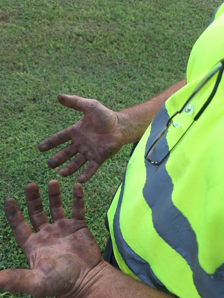 Grease-marked hands beside a high-visibility work shirt